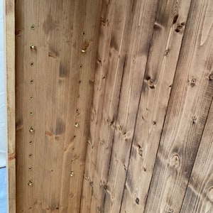 May include: The interior of a wooden cabinet with a series of brass hooks along the side. The wood is a light brown color and has a natural finish.