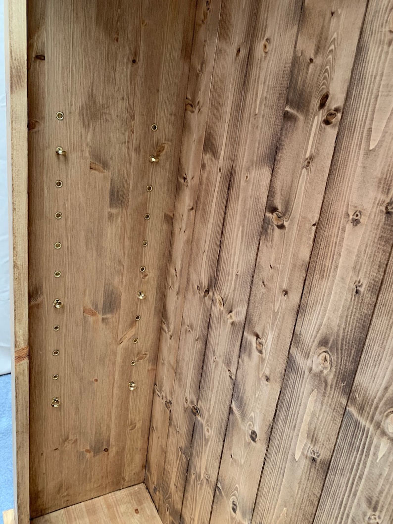 May include: The interior of a wooden cabinet with a series of brass hooks along the side. The wood is a light brown color and has a natural finish.