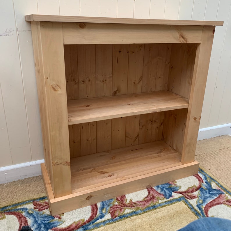 May include: A natural wood bookshelf with two shelves. The bookshelf has a simple design with a base and a top trim.