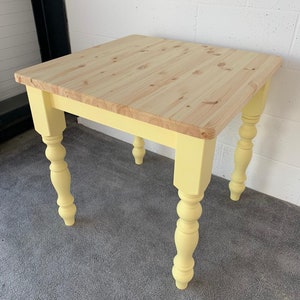 May include: A yellow painted square table with a natural wood top and turned legs. The table is sitting on a gray carpet.