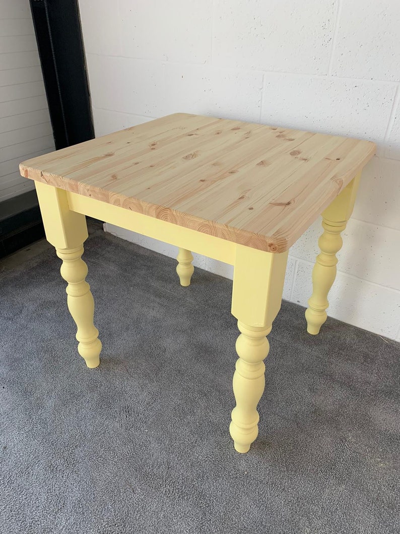 May include: A yellow painted square table with a natural wood top and turned legs. The table is sitting on a gray carpet.