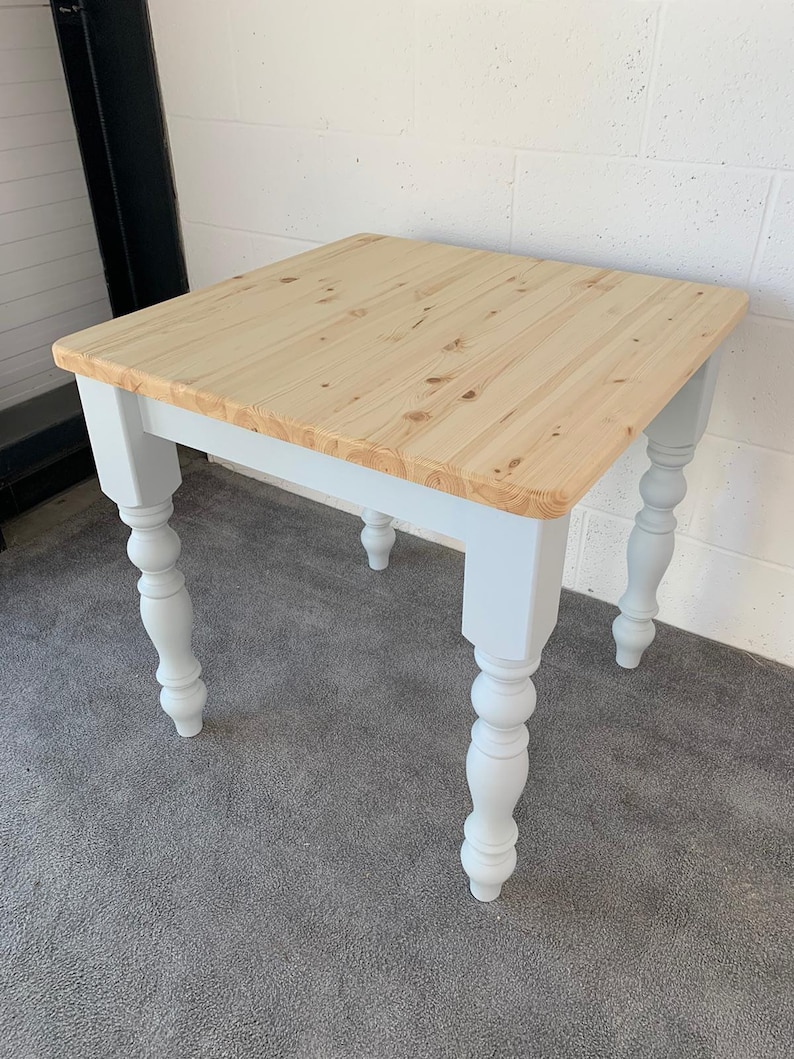 May include: A square wooden table with a light wood top and white painted legs. The legs have a turned design.