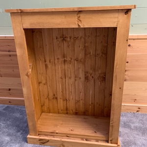 May include: A wooden cabinet with a single shelf and a closed door. The cabinet is made of unfinished pine wood and has a natural wood color.