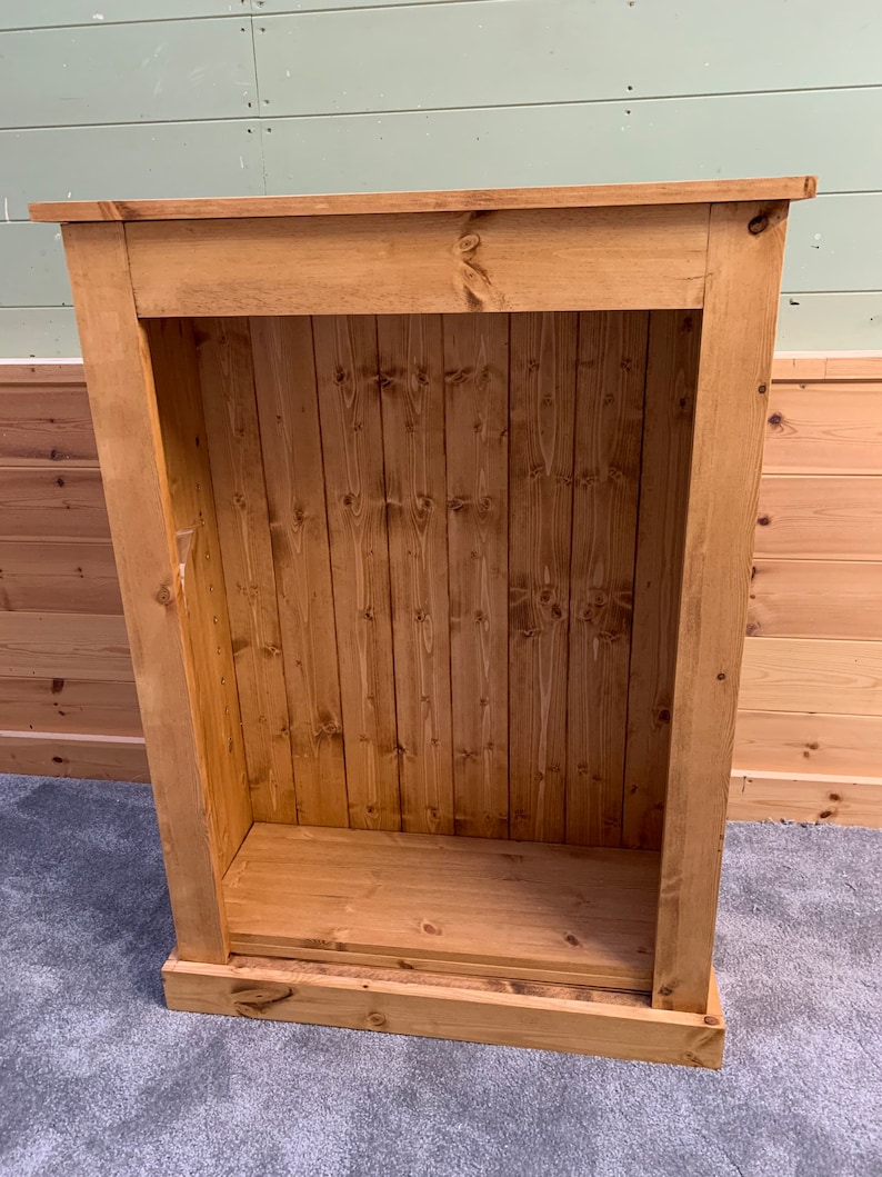 May include: A wooden cabinet with a single shelf and a closed door. The cabinet is made of unfinished pine wood and has a natural wood color.