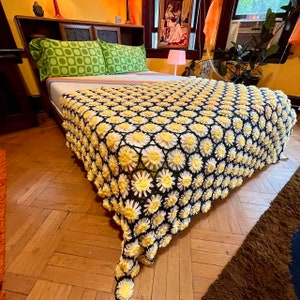 May include: A white bed with a yellow and green crocheted daisy blanket. The bed has a wooden headboard and footboard. The blanket is made of crocheted flowers.