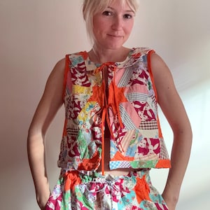 May include: A patchwork vest and matching shorts set. The vest is sleeveless with a round collar and orange trim. The patchwork design features various fabric patterns in red, orange, green, and blue. The shorts have a drawstring waist and a similar patchwork design.