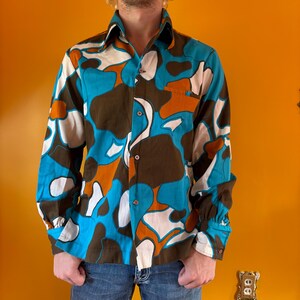 May include: A long-sleeved shirt with a colorful abstract pattern in shades of blue, brown, orange, and white.