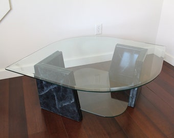 May include: A glass coffee table with a curved top and a black marble base. The table has a modern design and is perfect for a living room or den.