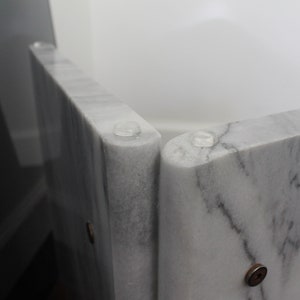 May include: Close-up of a white marble table with clear rubber feet. The table is made of several pieces of marble that are joined together.