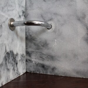 May include: A close-up of a silver shower arm mounted to a white marble wall.