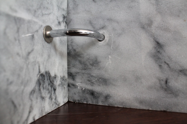 May include: A close-up of a silver shower arm mounted to a white marble wall.