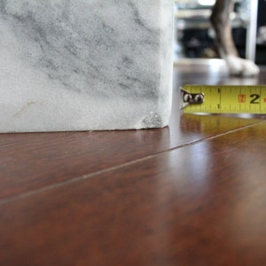 May include: Close-up of a white marble block with a measuring tape reading "2" inches. The marble block is sitting on a wooden surface.