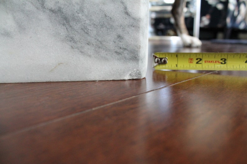 May include: Close-up of a white marble block with a measuring tape reading "2" inches. The marble block is sitting on a wooden surface.