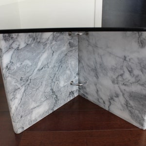 May include: A glass-top coffee table with a white marble base. The base is made of four pieces of marble that meet in the center, creating a unique and modern design.