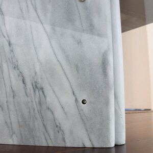 May include: A white marble table base with a curved design and two visible screw holes.
