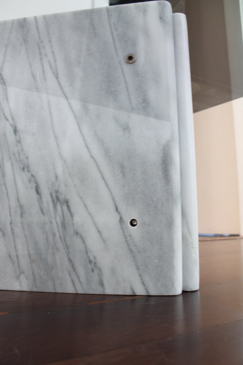 May include: A white marble table base with a curved design and two visible screw holes.