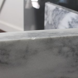May include: Close-up of a white marble countertop with a small chip on the edge.