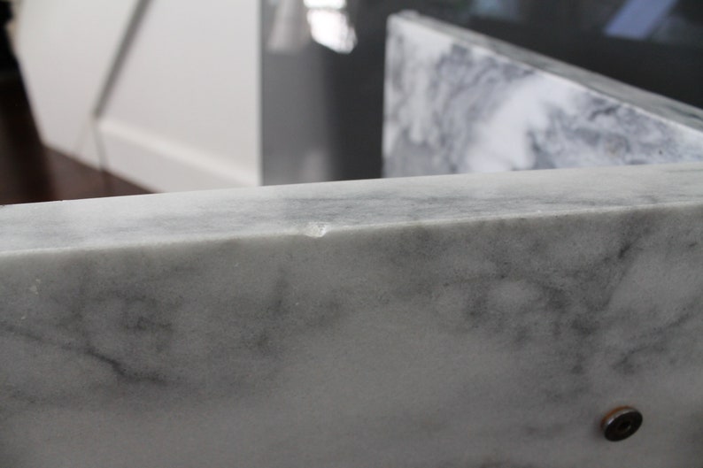 May include: Close-up of a white marble countertop with a small chip on the edge.
