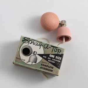 May include: A pink and silver vintage atomizer with a stretch cap. The box reads "Stretch-Cap Spray-A-Top Model 5-50 One Size Fits All Cologne Bottles Makes a Complete Atomizer".