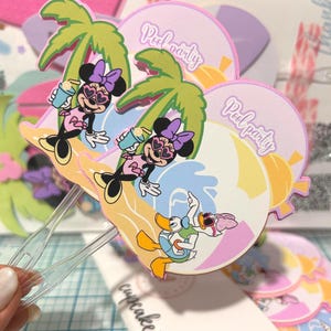 Puede incluir: Adornos coloridos para cupcakes con ilustraciones de Minnie Mouse y Donald Duck, palmeras y la frase "Pool Party". Los adornos están sujetos a palitos de plástico transparente, ideales para decorar cupcakes.