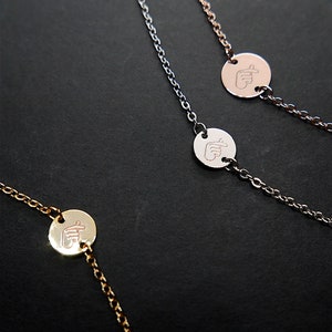 Op de afbeelding: Drie delicate kettingen met kleine ronde hangers met een handgebaar symbool. De kettingen zijn in zilver, goud en roségoud.