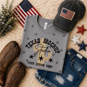 May include: A heather gray t-shirt with a repeating dark gray star pattern, featuring a central graphic of a tan cactus and the black text Texas Mockup Studio Your Design Here, accompanied by brown leather boots, denim shorts, and a flag cap.