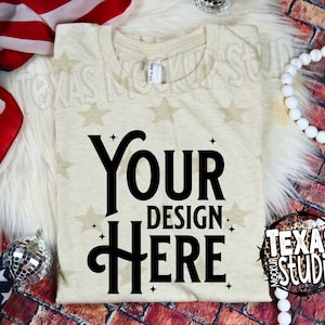 May include: A cream-colored t-shirt with the text "YOUR DESIGN HERE" in black. The shirt has a star pattern and is displayed with an American flag and decorative beads. The image is a mockup for a t-shirt design.
