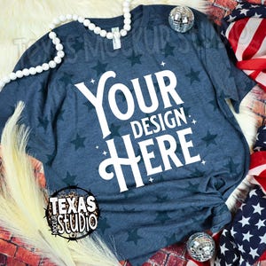 May include: A navy blue t-shirt with a star pattern and the text "YOUR DESIGN HERE" in white. The shirt is displayed with decorative elements including a string of white beads, a disco ball, and an American flag.