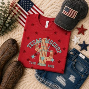 May include: A red t-shirt with a cactus graphic and the text "TEXAS MOCKUP STUDIO YOUR DESIGN HERE" in teal, surrounded by dark red stars. The shirt is displayed with a charcoal baseball cap featuring an American flag patch, brown cowboy boots, and blue denim shorts.