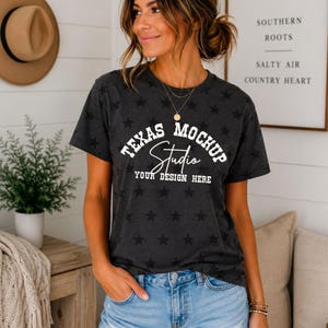 May include: A dark charcoal gray short-sleeve t-shirt featuring an all-over black star pattern. The front displays white text reading TEXAS MOCKUP, with the word Studio in a cursive script below, and the text YOUR DESIGN HERE at the bottom.