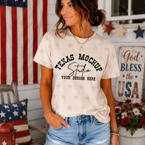 May include: A beige short-sleeve t-shirt with a repeating light brown star pattern. The center features black text reading TEXAS MOCHUP, a script font reading Studio, and the text YOUR DESIGN HERE in a bold, blocky font style.