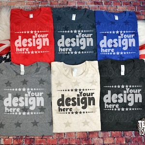 May include: Six folded t-shirts in red, navy, blue, gray, cream, and charcoal. Each shirt has the text "Your design here" in white. The shirts are arranged on a brick surface with an American flag.