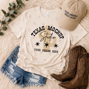 May include: A cream-colored t-shirt with a faint star pattern, featuring the black text "TEXAS MOCKUP STUDIO" and "YOUR DESIGN HERE" with a cactus graphic. Accompanied by a tan baseball cap with "MAKE AMERICA GREAT AGAIN" text, blue denim shorts, and brown leather cowboy boots.
