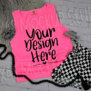 May include: A neon pink tank top with the text "Your Design Here" in black script. The image also includes black and white checkered shorts, a black beaded necklace, a hair clip, and a checkered scrunchie.