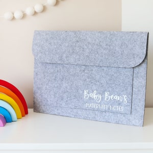 May include: Gray felt folder with the text "Baby Bean's Maternity Notes" in white lettering.