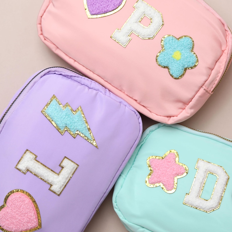 May include: Three pastel-coloured zippered pouches. The pink pouch has a large letter "P" and a flower patch. The purple pouch has a letter "L" and a lightning bolt patch. The aqua pouch has a letter "D" and a star patch. All patches have gold trim.