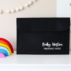 Könnte beinhalten: Schwarze Filzmappe mit dem Text "Baby Weston Pregnancy Notes" in weißen Buchstaben.