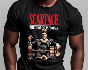 May include: Black t-shirt with a red graphic of a man in a suit holding a glass of whiskey and a cigar. The graphic says "Scarface" and "The World Is Yours".