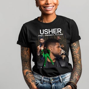 Può includere: Maglietta nera con una grafica di Usher, che presenta immagini di lui in diverse epoche della sua carriera. Il testo "USHER PAST, PRESENT, FUTURE" è stampato sulla maglietta.
