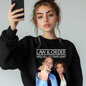 May include: A black sweatshirt with a white graphic print of the text "Law & Order Special Victims Unit" and a photo of two people giving the middle finger.