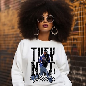 Puede incluir: Sudadera blanca con un estampado gráfico en blanco y negro de un hombre con una chaqueta azul y pantalones vaqueros. El texto gráfico dice "They Not Like Us!"