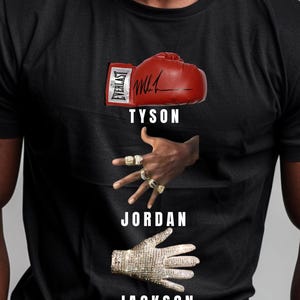 May include: Black t-shirt featuring a red boxing glove with "EVERLAST" and a signature, the word "TYSON", a hand with multiple rings, the word "JORDAN", and a jeweled glove with the word "JACKSON".