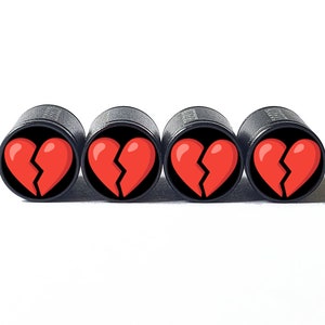 Puede incluir: Cuatro objetos cilíndricos negros con un diseño de corazón roto rojo sobre fondo negro. Los objetos están dispuestos en fila sobre un fondo blanco. El corazón roto es de color rojo brillante.