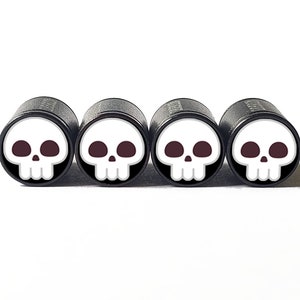 May include: Set of four black valve stem caps with white skull designs. Each cap features a white skull with black eyes and a black nose.