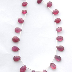 Könnte beinhalten: Eine Strähne rosafarbener Edelsteinperlen in Tropfenform. Die Perlen sind auf einem Silberdraht aufgefädelt.