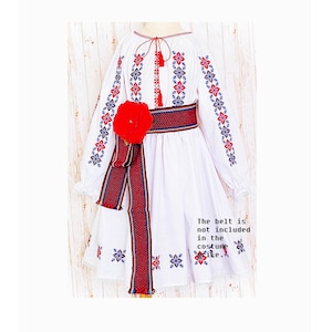 May include: White dress with red and blue floral embroidery on the sleeves and hem. A red belt with a matching floral design and a large red flower accentuates the waist. The text on the image says, "The belt is not included in the costume site."