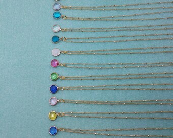 May include: A collection of gold-colored necklaces with various colored gemstone pendants. Each necklace features a delicate chain with small beaded accents. The gemstones are round and come in a variety of colors, including red, blue, and green.
