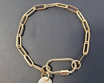 May include: Gold-coloured chain bracelet featuring a carabiner clasp and a circular charm. The charm is white with a gold-coloured letter "M". The bracelet is displayed on a dark surface.