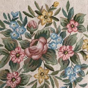 May include: A beige fabric with an embroidered floral design. The flowers are pink, red, blue, and yellow. The design is intricate and detailed.