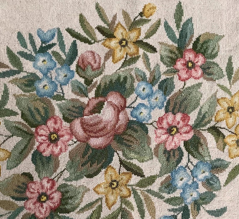 May include: A beige fabric with an embroidered floral design. The flowers are pink, red, blue, and yellow. The design is intricate and detailed.
